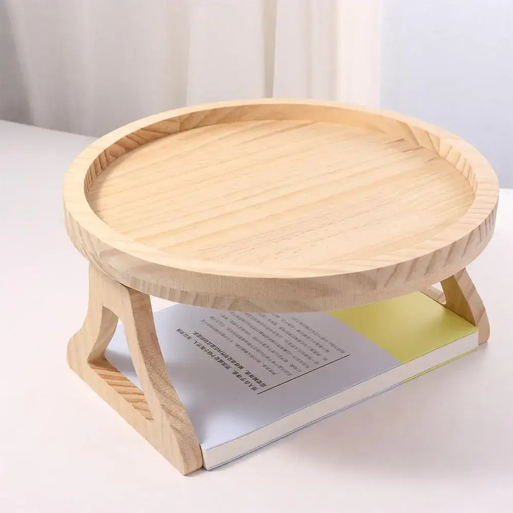 A round tray made from natural bamboo with ridged edges sits atop an open book. Supported by a wooden stand, it creates a small shelf area below. This versatile Natural Bamboo Sofa Tray complements any decor, its adjustable design ensuring both practicality and style on the book’s white cover with text.