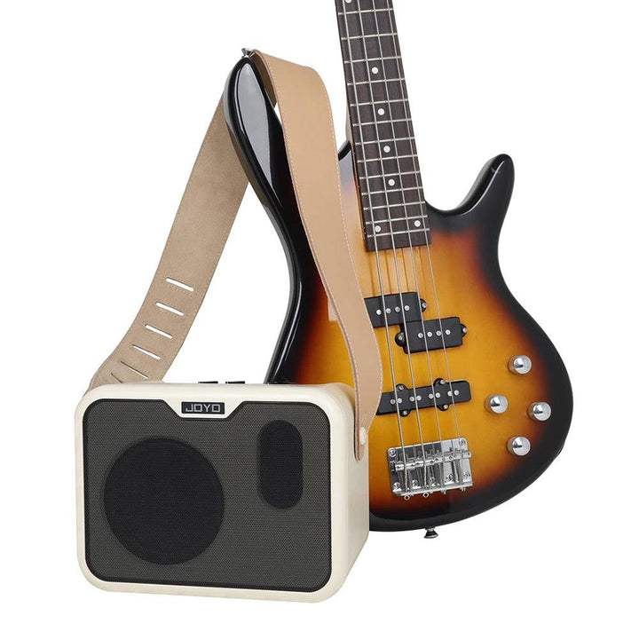 A sunburst electric bass guitar, a popular choice among bass guitarists, with a beige strap leans against the Portable Electric Bass Amplifier Rechargeable AMP Speaker, which is small, rectangular and black and beige, harmoniously showcasing musical instrument accessories.