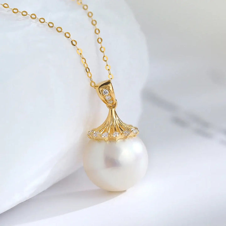 The 18K Gold Natural Fresh Water Pearl Necklace radiates elegance with its charming pendant. Featuring a decorative gold cap embellished with sparkling crystals arranged like a flower, this exquisite piece epitomizes the sophistication of women’s pendant jewelry against its blurred white backdrop.