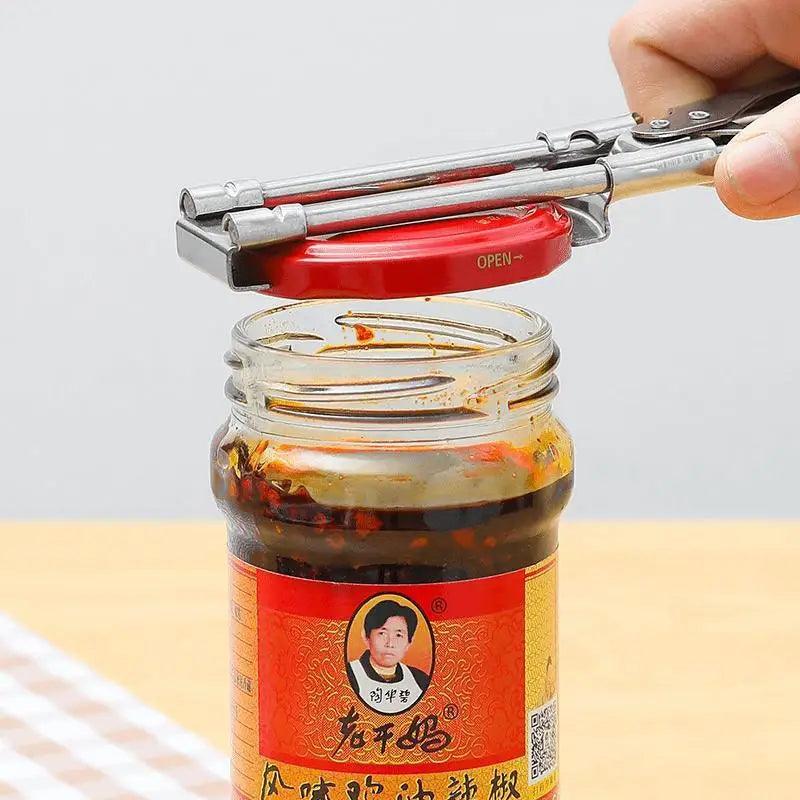 A hand using the Stainless Steel Adjustable Multi-Function Jar Opener - Effortless Kitchen Tool for Lids, Cans, and Bottles easily removes the red lid from a jar of Chinese chili paste, revealing the spicy contents inside. The jar is adorned with a red and yellow label featuring an image of a person.