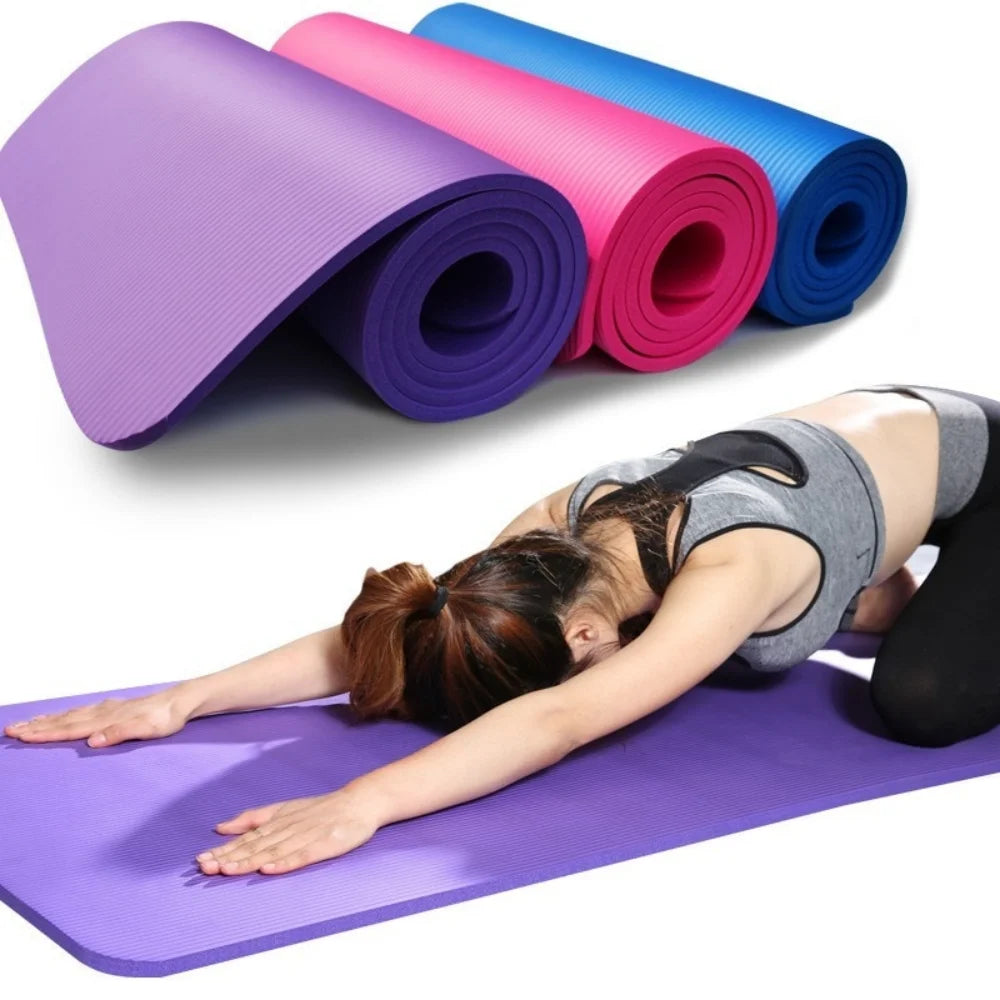 A person stretches in child's pose on an Anti-Skid Yoga Mat Thick EVA Comfort Foam Non-Slip Surface in purple. Three rolled yoga mats, available in purple, pink, and blue, are stacked behind them. The non-slip surface ensures stability as they flow seamlessly while wearing a gray sports bra and black leggings.