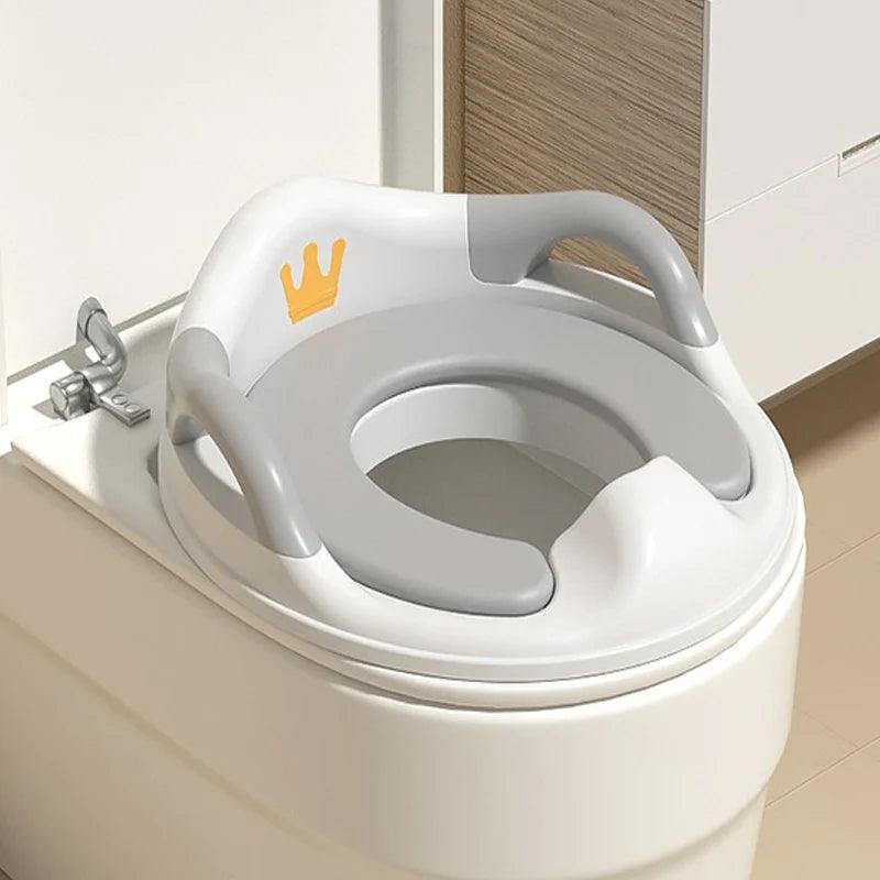 A gray and white Portable Potty Training Seat, designed with a small crown and a whimsical cartoon pattern, is positioned on a toilet. This Children's WC Seat offers armrests for extra support, making it ideal for kids learning the ropes of potty training.