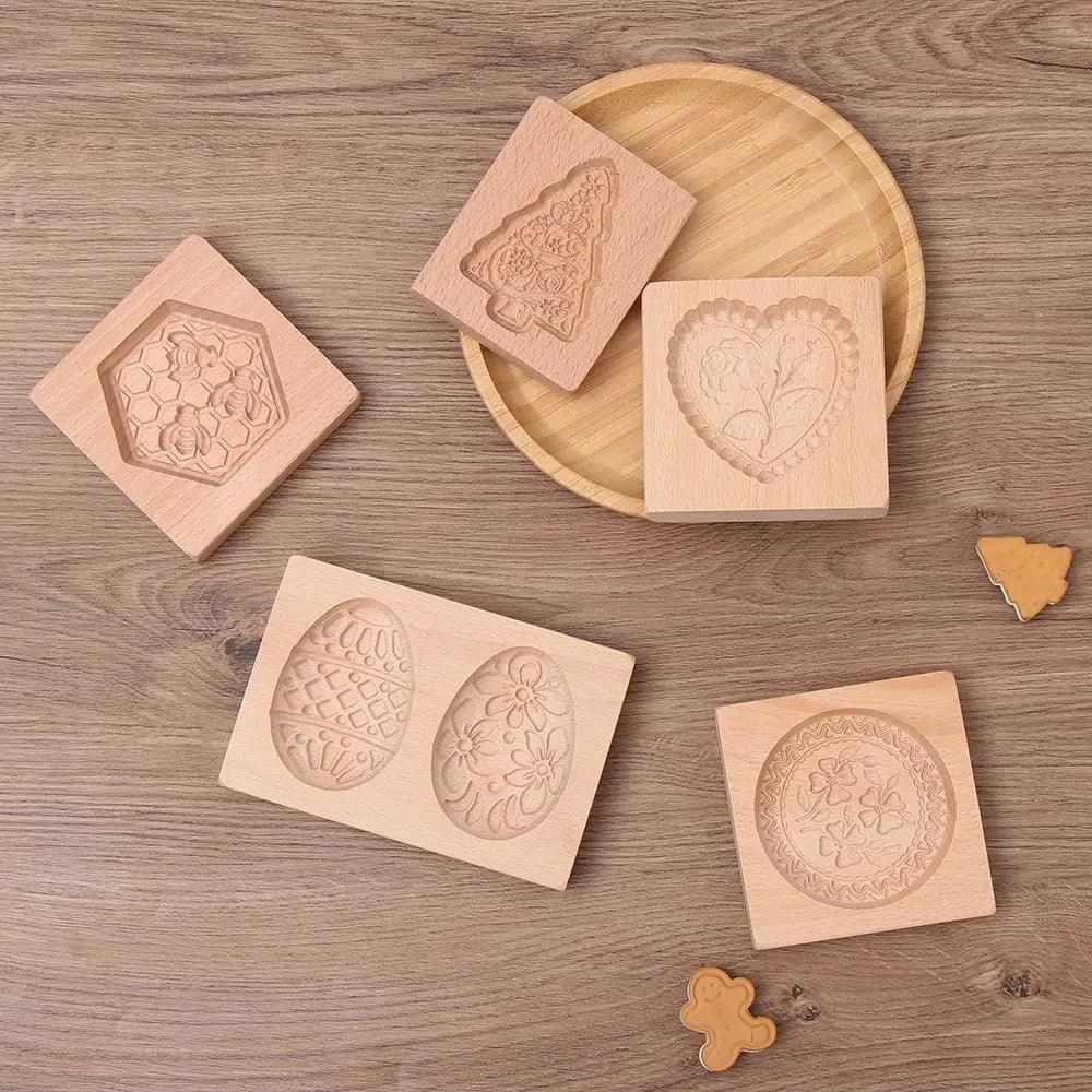 Displayed on a wooden surface are 3D wooden cookie molds featuring various designs such as a heart, tree, eggs, flowers, and circular patterns. An eco-friendly 3D wooden cookie mold enhances baking creativity alongside a round tray and a small gingerbread figure.