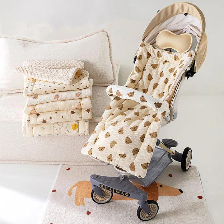 A beige baby stroller, featuring an ergonomic design and adorned with a teddy bear pattern, is parked on a carpeted floor. Next to it lies a stack of coordinating blankets. The room exudes a cozy, neutral-toned aesthetic with a plush couch in the background.