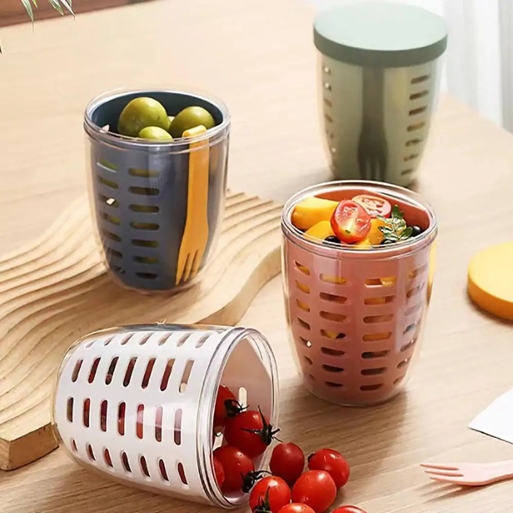 A collection of vibrant "Fruit Cup with Fork" containers is displayed on a wooden table, featuring an eco-friendly design. Some have lids, while others are open, revealing olives and cherry tomatoes. A small orange fork accompanies the setup, and one container is tipped over with tomatoes spilling out.