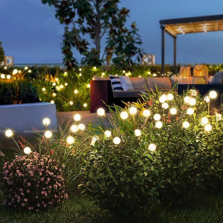 As the sky transitions to a deep blue, a cozy outdoor garden scene at dusk showcases "Warm white solar lights" expertly scattered among lush greenery and flowers. In the background, comfortable seating is nestled under a pergola, enhanced by the gentle glow of LED bulbs. This setup ensures reliable IP44 waterproof protection provided by "Outdoor solar lights.