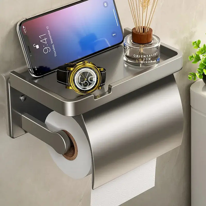 The Bathroom Tissue Holder Wall-Mounted Aluminum Holder is a rust-resistant toilet paper storage rack with a top shelf for your smartphone, watch, and reed diffuser. It's perfect for keeping essentials within reach while the roll hangs neatly below.