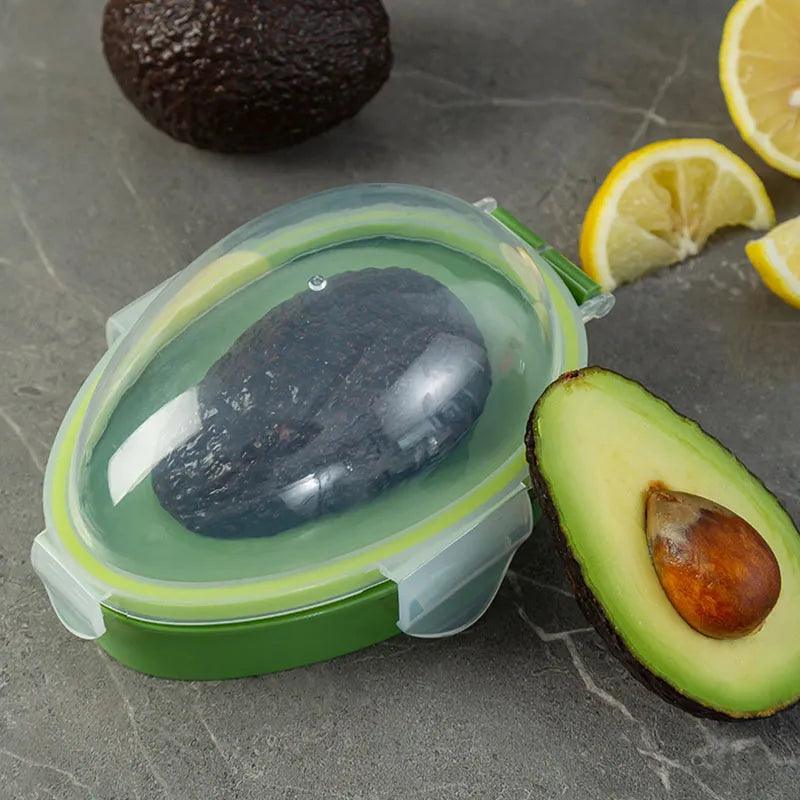 A halved avocado is nestled in a green Avocado Crisper Box Airtight storage container with a clear lid, while the seed-intact half is displayed on a gray surface nearby. Lemon wedges serve as a garnish for this Fresh Avocado Keeper ensemble.