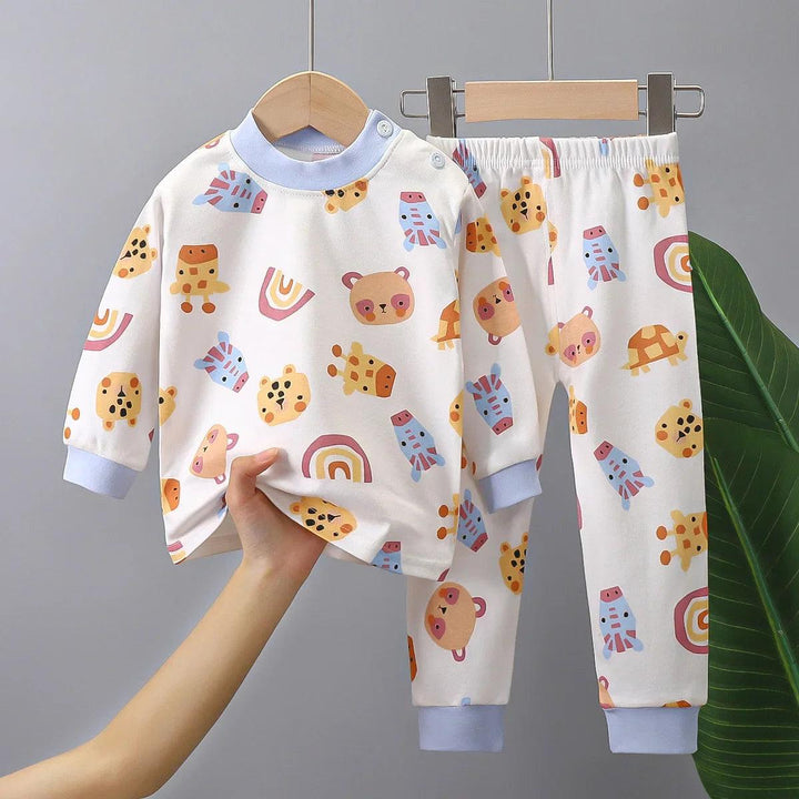 The Kids Pajamas Cartoon Dinosaur Toddler Clothing Sets are a vibrant wardrobe essential, showcasing playful designs of bears, rainbows, turtles, and cartoon dinosaurs. The charming patterns decorate both the top and pants, which are gracefully displayed on a wooden hanger against a gray backdrop with a green leaf peeking into the scene.