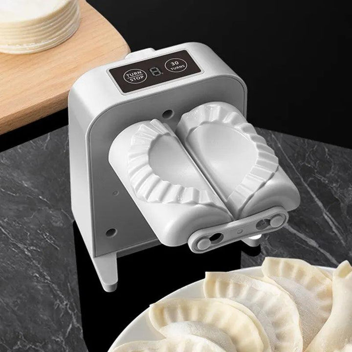 An elegant Automatic Dumpling Making Machine, designed for pressing dumplings and empanadas, rests on a black marble surface with unfilled wrappers nearby. The electric kitchen tool displays two partially sealed dumplings inside, poised for completion. A wooden board in the background holds additional wrappers to streamline the dumpling-making process.