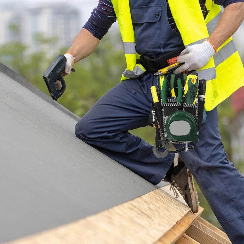 A person in a high-visibility vest is working on a roof, holding a tool while kneeling. Their Multifunctional Tool Bag Electrician Waist Pocket Portable Tool Pouch, designed for organized storage, carries various instruments. The blurred background features greenery and buildings.