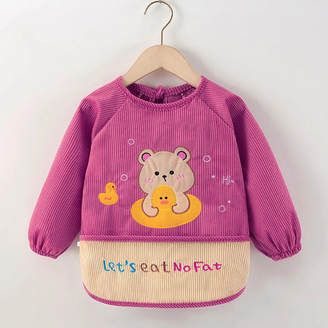 The Kids' Waterproof Eating Apron, designed as a cute toddler bib, offers a stylish look with its pink long-sleeve pullover featuring an adorable bear and duck design on the chest. The beige bottom is adorned with the colorful text "Let's eat No Fat.” Perfectly showcasing on a wooden hanger, this apron is made from waterproof polyester to handle those unavoidable spills.