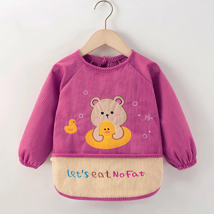 The Kids' Waterproof Eating Apron, designed as a cute toddler bib, offers a stylish look with its pink long-sleeve pullover featuring an adorable bear and duck design on the chest. The beige bottom is adorned with the colorful text "Let's eat No Fat.” Perfectly showcasing on a wooden hanger, this apron is made from waterproof polyester to handle those unavoidable spills.