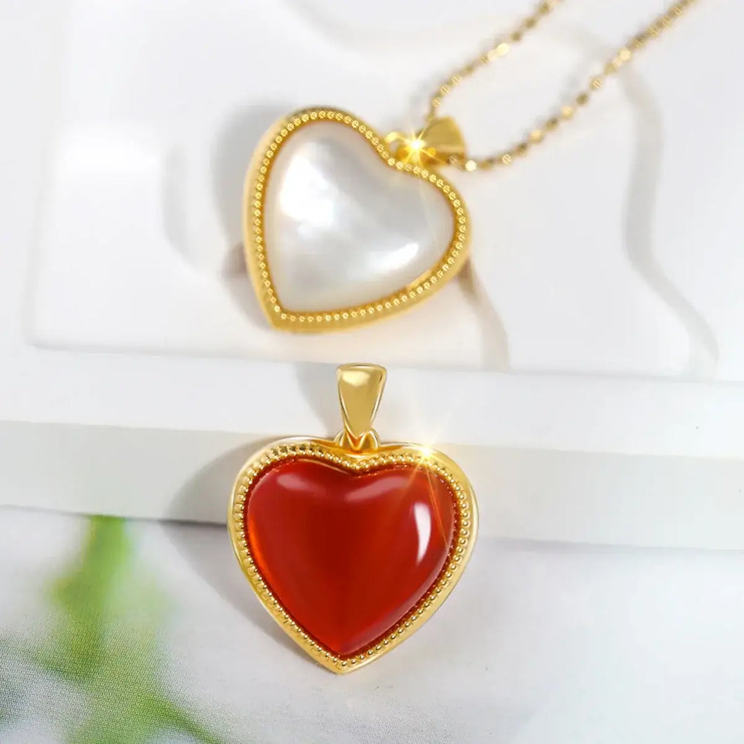 Displayed against a white background are two heart-shaped pendants from the Gold 18K Natural Agate Necklace for Women collection. One pendant features a striking red agate with a gleaming, shiny surface, while the other has a pearly white finish. Both are encased in elegant 18K gold borders, making them perfect pieces of wedding jewellery.