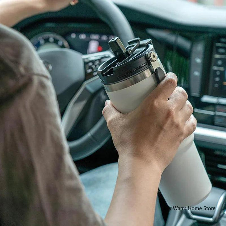 A person holding a Stainless Steel Thermos Insulated Travel Mug Vacuum Insulated Bottle in a car, with one hand on the steering wheel. The dashboard and part of the car's interior are visible.