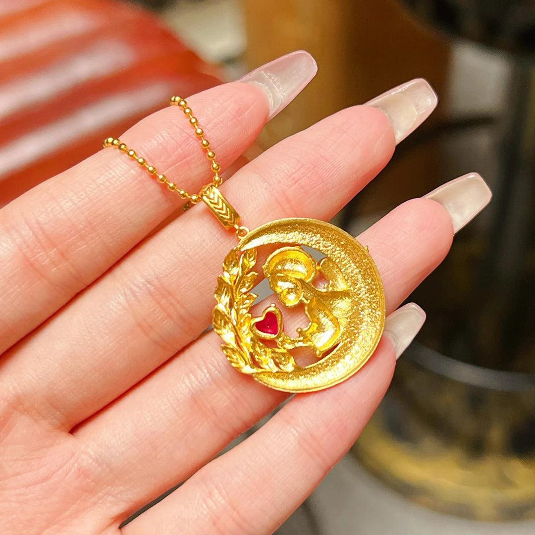 A person holds a luxurious 18K Gold Angel Necklace Initial Pendant, which features an embossed figure and a red heart on a round pendant. The piece dangles from a sterling silver chain, enhancing its charm, while the intricate border beautifully complements the person's long, manicured nails.