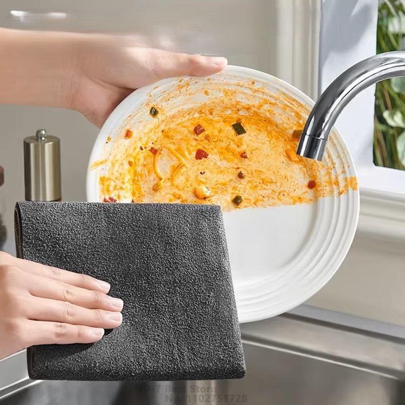 A person holds a white plate with food residue under a running faucet. They use a dark gray sponge and the Magic Cleaning Cloth Microfiber Glass Clean Towel Lint-Free Cleaning Rags to clean the plate. Sunlight streams in through the window, highlighting the lint-free cleaning process.